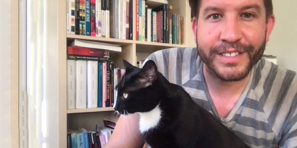 Man sitting in front of book shelf with his cat in his lap